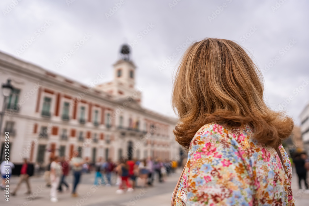 Tourist woman with her back looking at the clock tower of the Puerta del Sol buildings in Madrid. Tourist woman with her back looking at the clock tower of the Puerta del Sol buildings in Madrid.