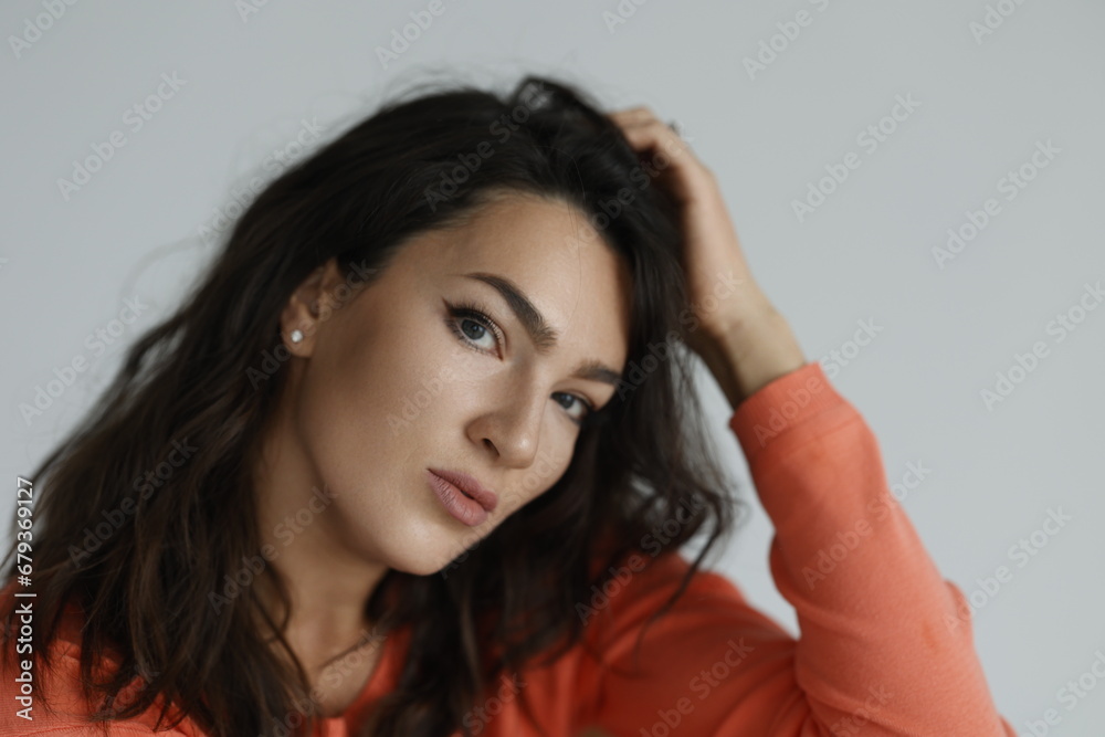 Beautiful woman of 30 years old sitting on chair, white background. Portrait of brunette girl smile. Orange sweater and light jeans. Woman barefeet, thoughtful. Beautiful woman of 30 years old sitting on chair, white background. Portrait of brunette girl smile. Orange sweater and light jeans. Woman barefeet, thoughtful.