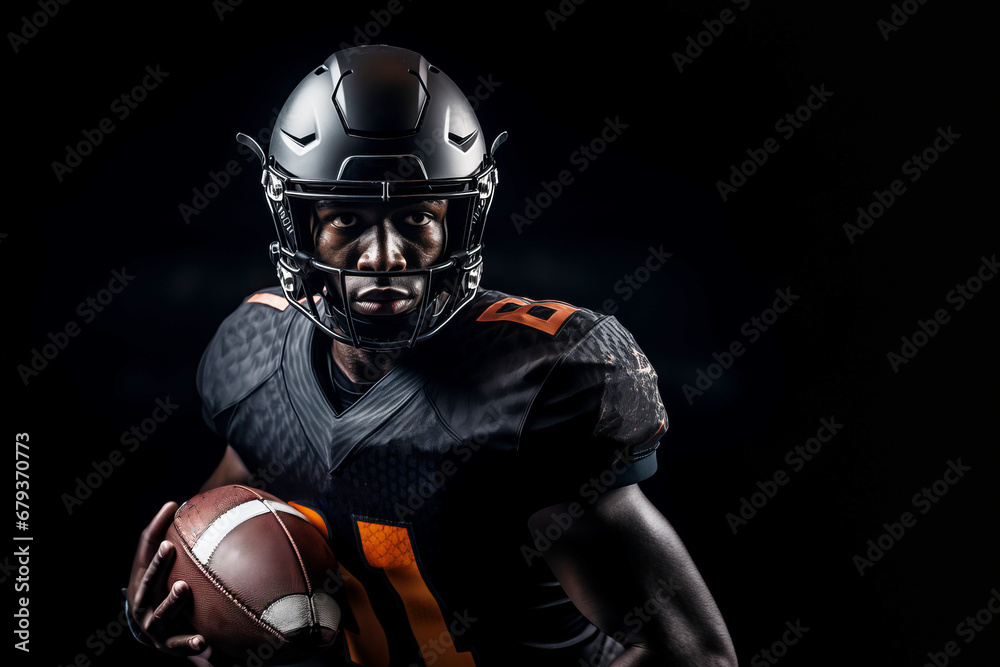 Studio shot of professional American football player in black jersey holding ovoid ball in his hand. Determined, powerful, skilled African American athlete wearing helmet. Isolated in black background