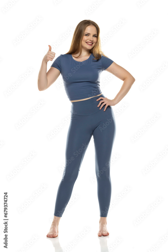 Full body, front view young smiling woman in sportswear posing on white background and showing thumbs up Full body, front view young smiling woman in sportswear posing on white background and showing thumbs up