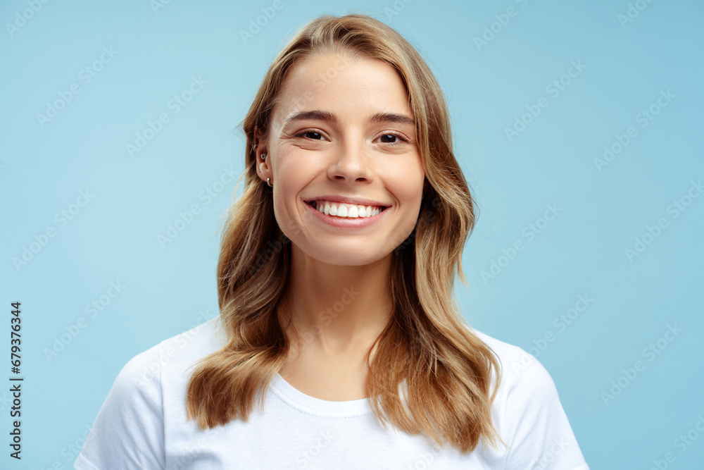 Portrait of beautiful smiling woman with toothy smile looking at camera isolated on blue background, dental concept. Attractive gorgeous fashion model with silky wavy hair posing in studio Portrait of beautiful smiling woman with toothy smile looking at camera isolated on blue background, dental concept. Attractive gorgeous fashion model with silky wavy hair posing in studio