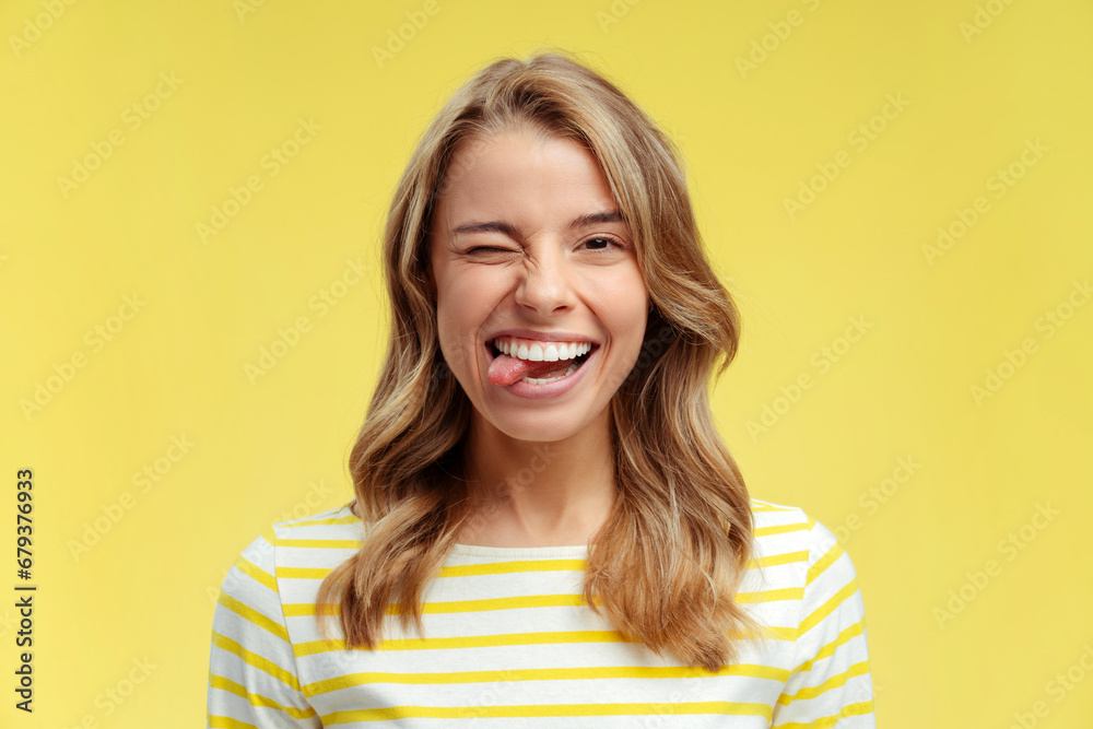 Portrait of attractive happy woman with toothy smile showing tongue looking at camera standing isolated on yellow background. Positive lifestyle concept Portrait of attractive happy woman with toothy smile showing tongue looking at camera standing isolated on yellow background. Positive lifestyle concept