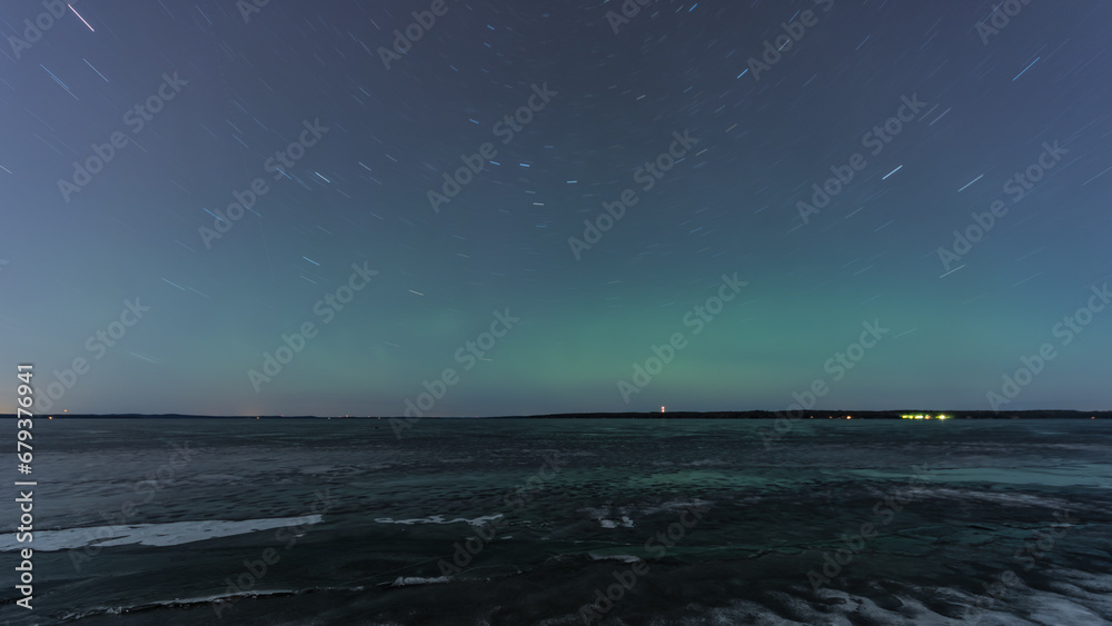 Green aurora borealis hue and rotating stars over a frozen lake in Tampere, Finland