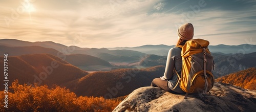 Back view young woman wearing a backpack and sit on stone in mountain at sunset photo