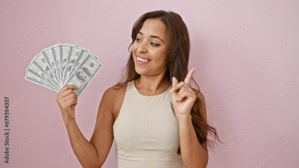Eureka moment for young, beautiful hispanic woman holding dollar banknotes! pointing her finger to showcase a smart idea number one, over an isolated pink background with a delighted, confident smile. Eureka moment for young, beautiful hispanic woman holding dollar banknotes! pointing her finger to showcase a smart idea number one, over an isolated pink background with a delighted, confident smile.
