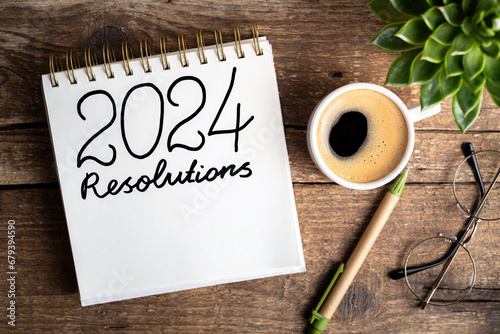 2024 New year resolutions on desk. 2024 goals list with notebook, coffee cup, plant on wooden background. Resolutions, plan, goals, action, strategy, success concept. New Year 2024 resolutions