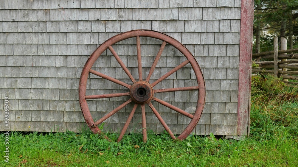 an old wooden wheel leaning against a barn in front of grass