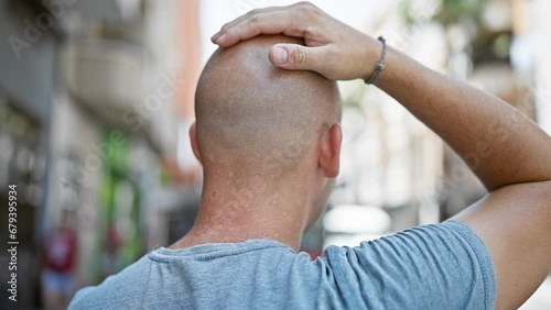 Young hispanic man standing backwards touching head at street