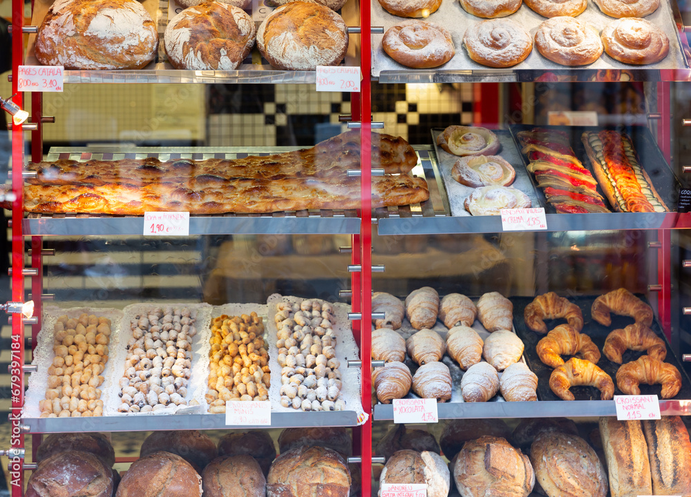 Spanish bakery showcase with freshly baked bread and various appetizing sweet confectioneries. Price tags with product names in Catalan.