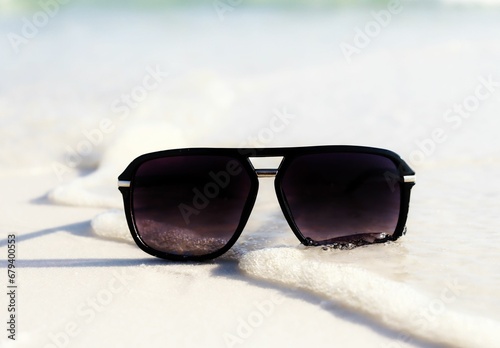 black glasses are laying on the sand near the ocean waves