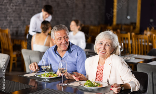 Smiling senior man and woman talking and joking merrily during dinner in restaurant. Elderly spouses colleagues have fun chatting spend time in restaurant after working day