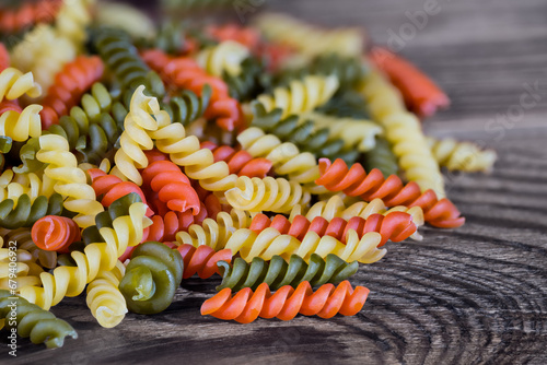 Heap of yellow, red and green fusilli pasta of helical shape on brown wooden background. Close-up a pile of raw colored egg rotini of tomato or spinach flavor. Staple food for Italian cuisine cooking. photo
