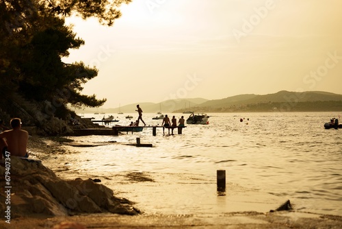 Fototapeta Naklejka Na Ścianę i Meble -  Group of people enjoying a sunny day by the water at sunset in Trogir, Croatia