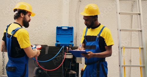 Expert technicians team working with manifold gauges to check air conditioner refrigerant levels, writing result on clipboard. Skillful mechanics using barometer benchmarking hvac system tool