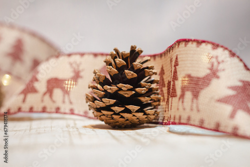 Pine cone wrapped in a festive ribbon with reindeer and tree designs and fairy lights