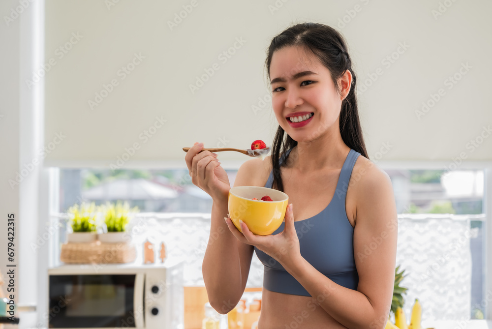 Beautiful Asian young female eating strawberry yogurt for health in the kitchen room at the apartment. Beautiful Asian young female eating strawberry yogurt for health in the kitchen room at the apartment.