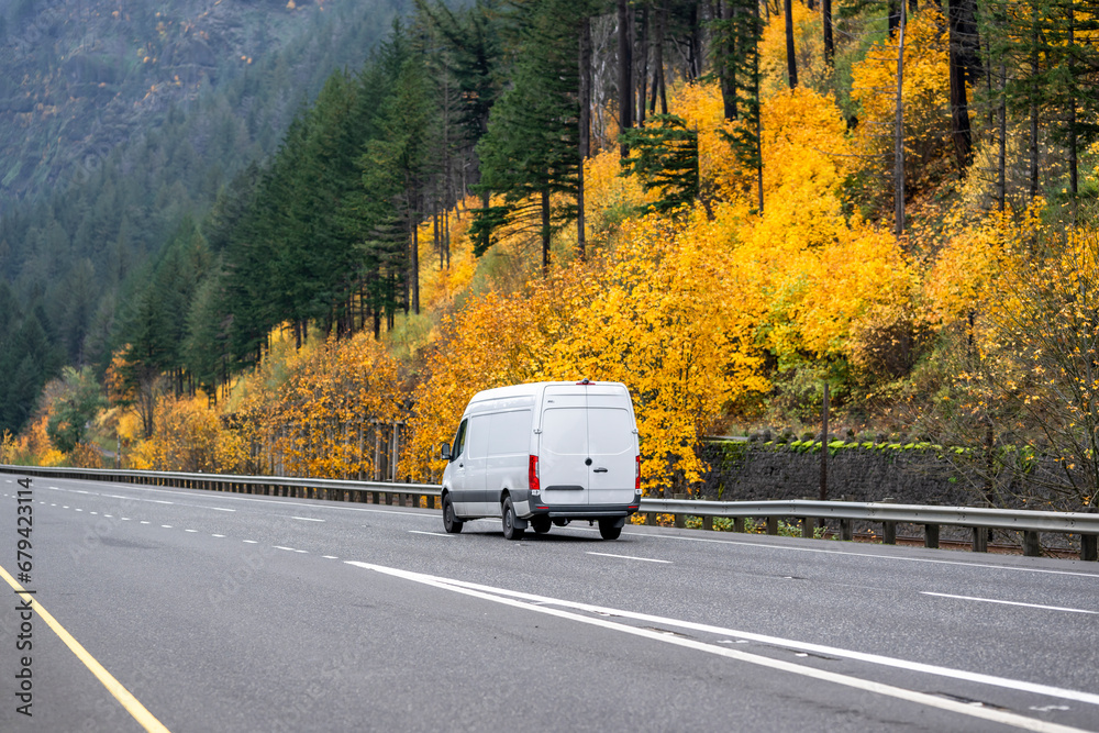 Cargo compact mini van driving on the scenic autumn highway road with yellow trees on the mountain hillside - obrazy, fototapety, plakaty 