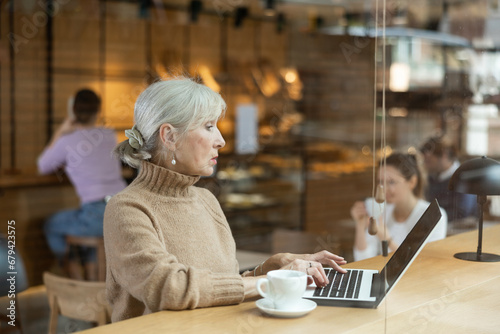 Confident senior female cafe customer enjoying peace and quiet while working on laptop