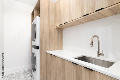 A laundry room with wood cabinets, a white marble countertop, patterned tile floor, and white washer and dryer. photo
