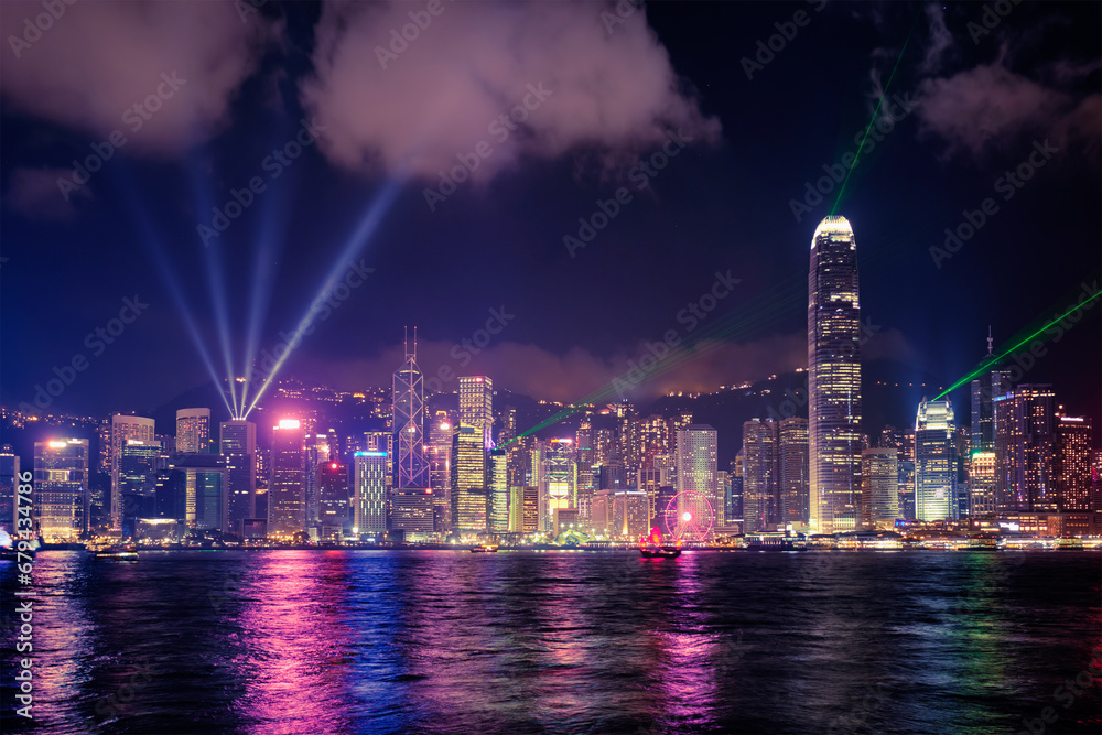 Hong Kong skyline cityscape downtown skyscrapers over Victoria Harbour in the evening illuminated with lasers with tourist boat and ferries . Hong Kong, China