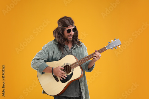 Stylish hippie man playing guitar on orange background