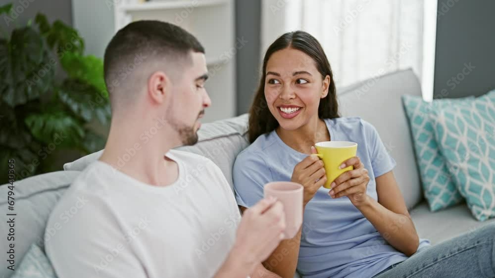 Beautiful couple sitting on sofa together drinking coffee at home Beautiful couple sitting on sofa together drinking coffee at home