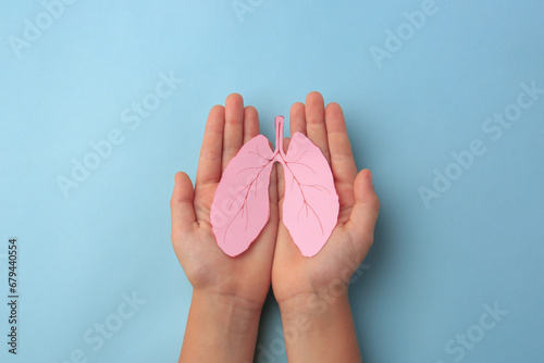 Child holding paper human lungs on light blue background, top view photo