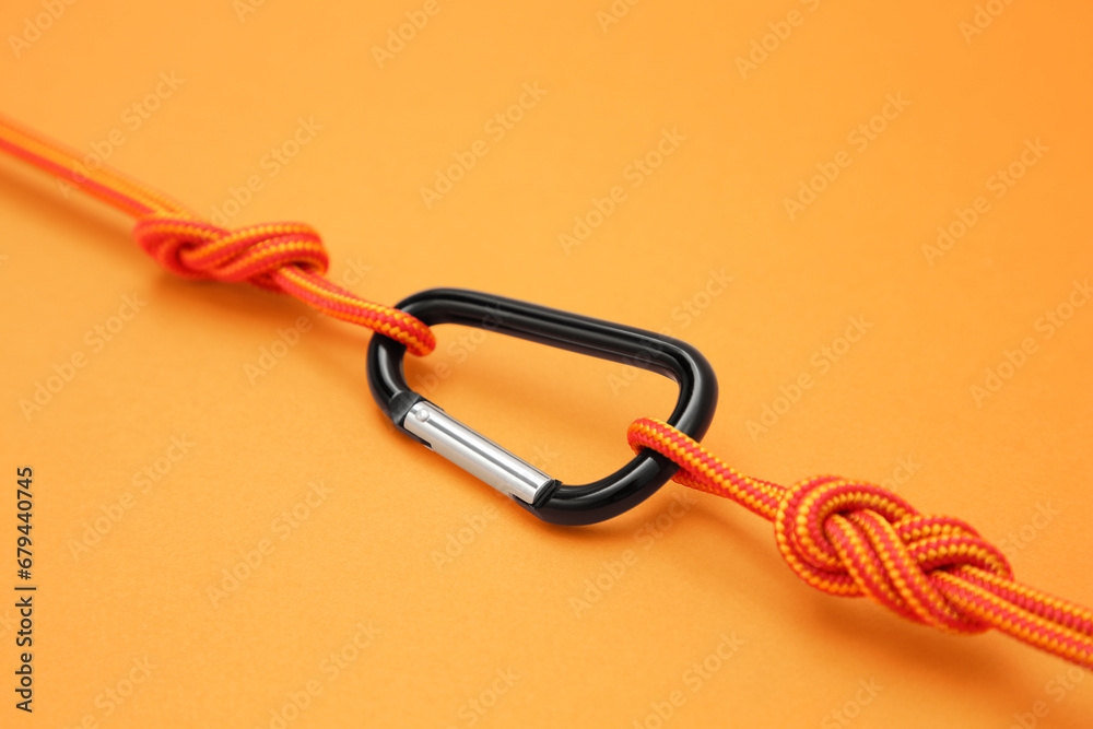 One metal carabiner with ropes on orange background, closeup One metal carabiner with ropes on orange background, closeup