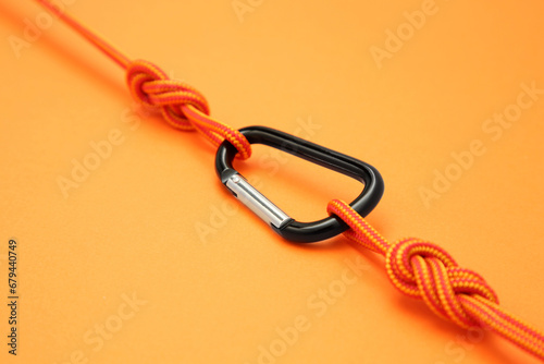 One metal carabiner with ropes on orange background, closeup