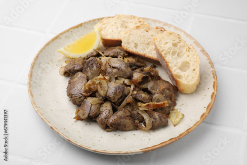 Tasty fried chicken liver served with lemon and bread on white tiled table, closeup