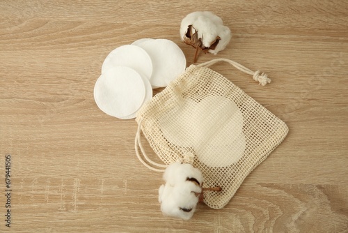 Cotton pads, bag and flowers on wooden table, above view. Space for text