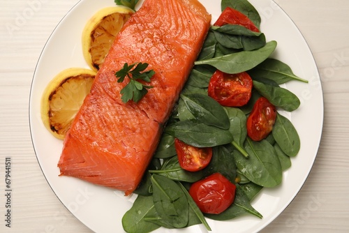 Tasty grilled salmon with basil, tomatoes and lemon on white wooden table, top view