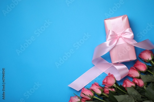 Beautiful gift box with bow and pink roses on light blue background  flat lay. Space for text