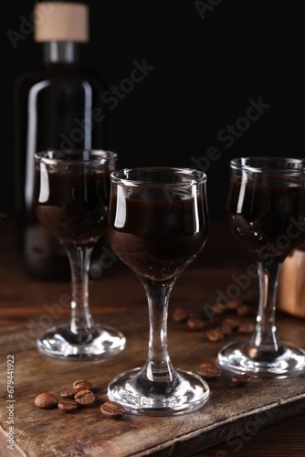 Shot glasses with coffee liqueur and beans on wooden table, closeup