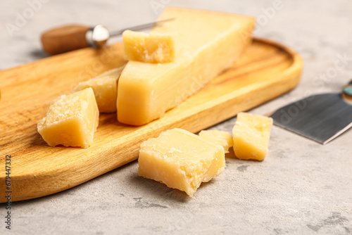 Wooden board with pieces of tasty Parmesan cheese on grunge background, closeup