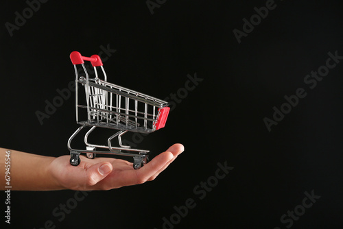 Female hand with red shopping cart on black background.