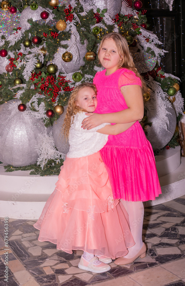 Beautiful elegant girls near the Christmas tree in the New Year. Holiday. New Year. Children are models. Two sisters. Beautiful elegant girls near the Christmas tree in the New Year. Holiday. New Year. Children are models. Two sisters.