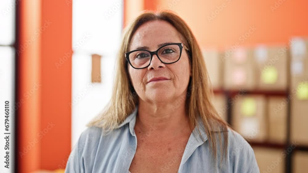 Middle age hispanic woman ecommerce business worker standing with serious face at office