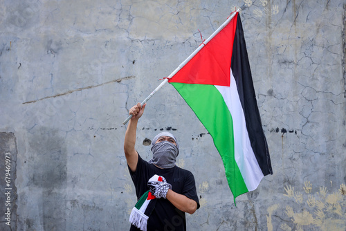 Young man waving the Palestine flag with hand on chest. photo