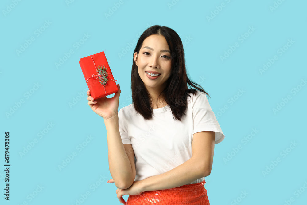Young Asian woman with Christmas gift box on blue background Young Asian woman with Christmas gift box on blue background
