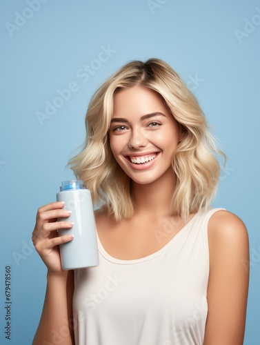 Smiling woman holding blank hygiene product bottle on blue backdrop.