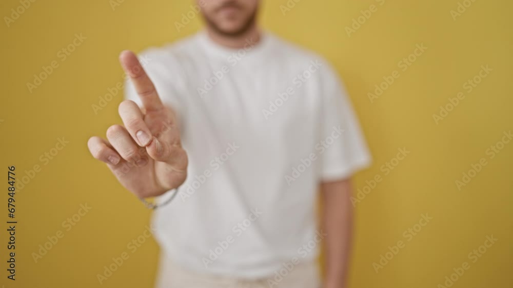 Young hispanic man saying no with finger over isolated yellow background