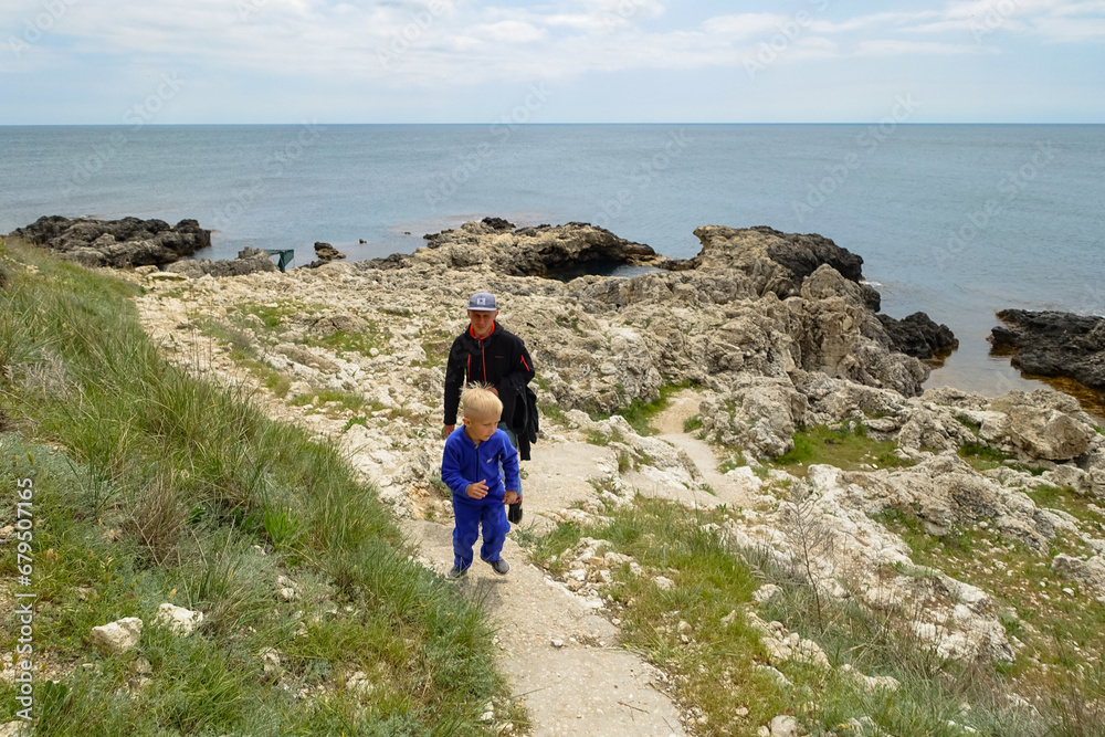 Fototapeta premium A man with a child on Cape Tarkhankut. The rocky coast of the Dzhangul Reserve in the Crimea. Turquoise sea water. Rocks and grottoes of Cape Tarkhankut on the Crimean peninsula.