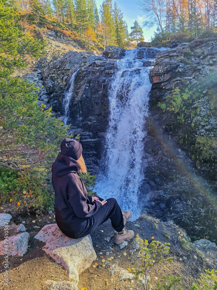 A girl on the background of a beautiful waterfall in the autumn mountains beyond the Arctic Circle in the north, in Khibiny, Murmansk region. Kola Peninsula