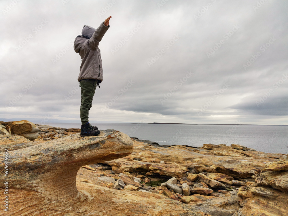 Obraz premium A boy on the shore of red stones next to the rocks of Two brothers on the Fishing Peninsula. The picturesque shore of the harsh Barents Sea. The North of Russia. The Kola Peninsula. The Arctic