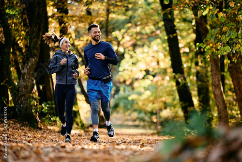 Happy athletic couple jogging through autumn park.