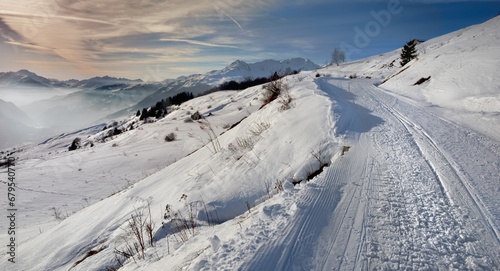 snowy footpath crossing alpine mountain with view to the valley and mountain range .