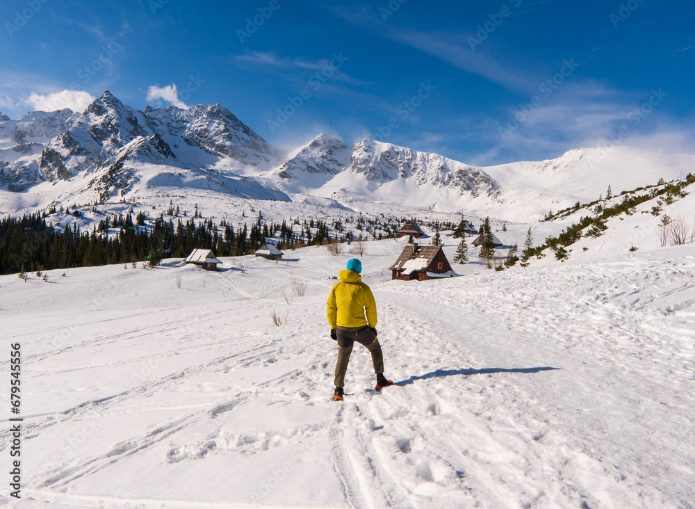 Hiker looking at a snowy mountain landscape in a sunny winter day. European hiking solo outdoor active healthy lifestyle. Outdoor healthy lifestyle concept. High Tatras mountain in slovakia nad poland