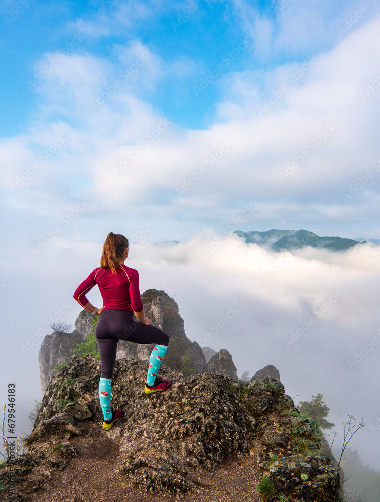 Woman hiker on a top of a mountain. Rear view of a young woman on a mountain top peacefully gazing at low-lying morning clouds and the pastel colours of a tranquil sunrise
