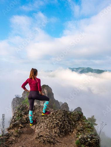 Obraz na płótnie Woman hiker on a top of a mountain. Rear view of a young woman on a mountain top peacefully gazing at low-lying morning clouds and the pastel colours of a tranquil sunrise w salonie
